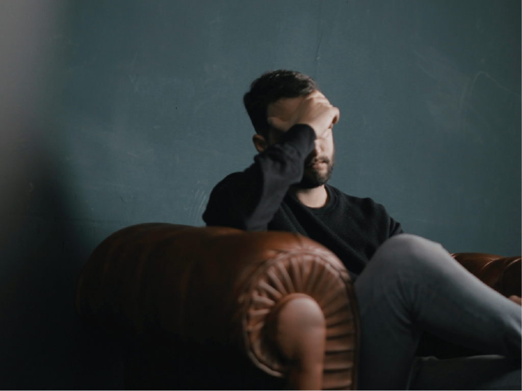 a man holds his head while sitting on a sofa